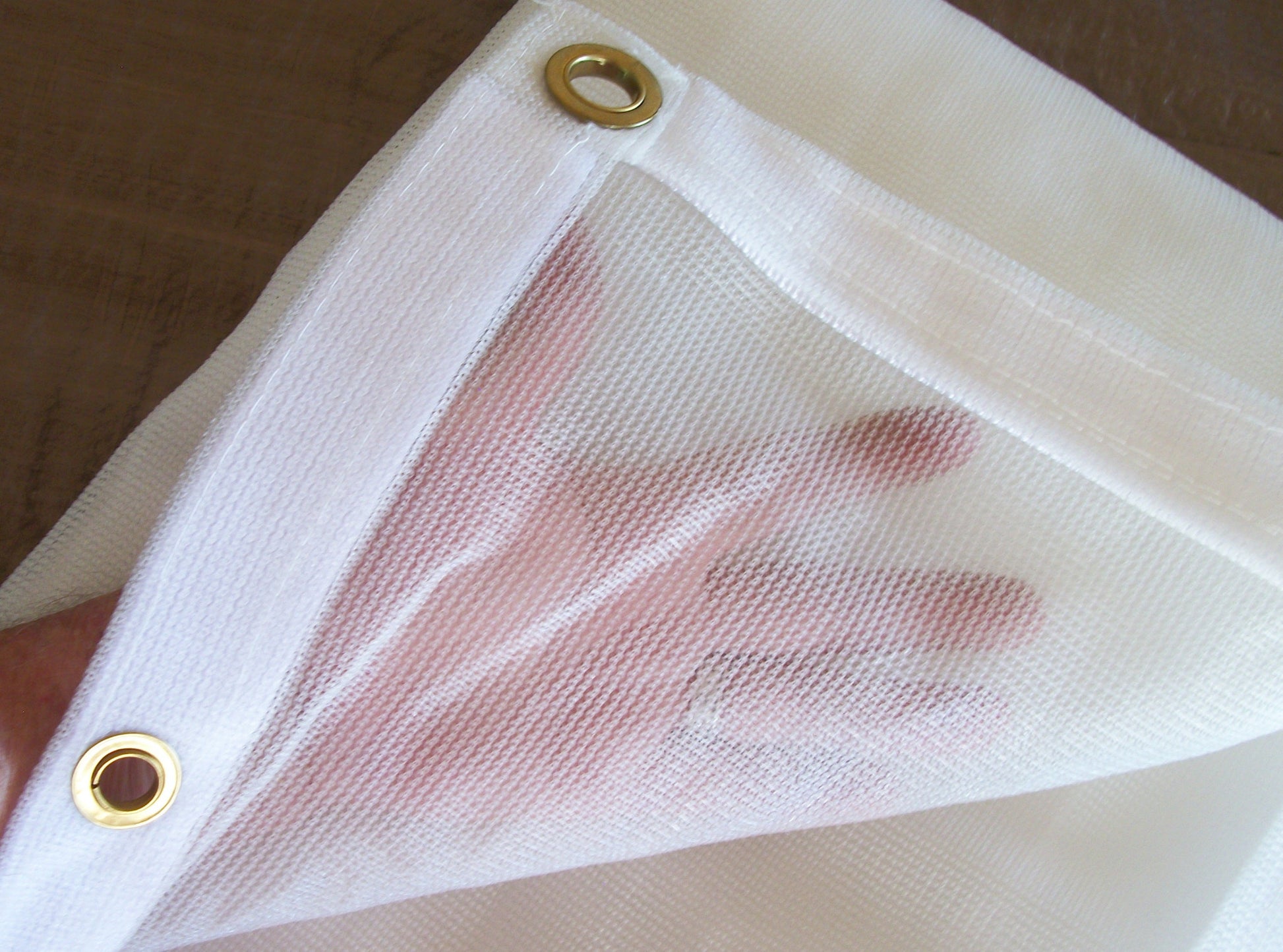 Close-up of breathable mesh tarp material showing weave pattern reinforced edge and grommet